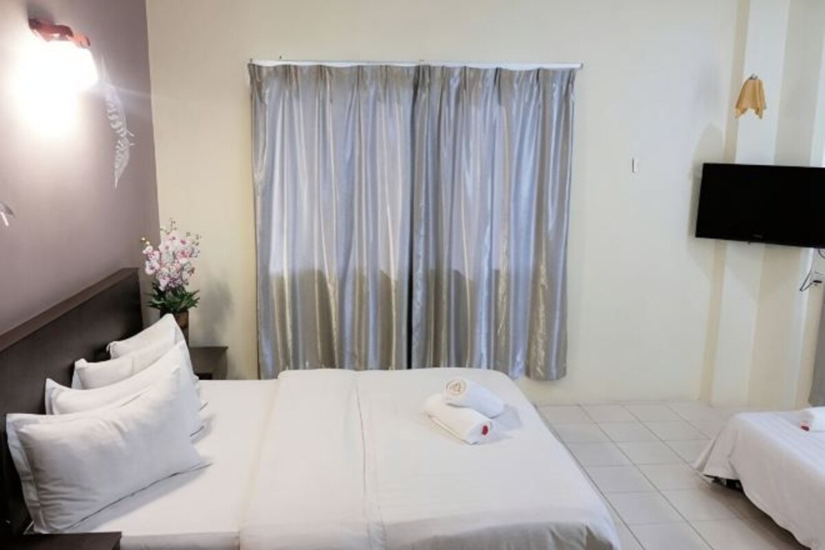 Une chambre d’hôtel avec un lit, une télévision, une fenêtre avec des rideaux et un téléviseur fixé au mur.
