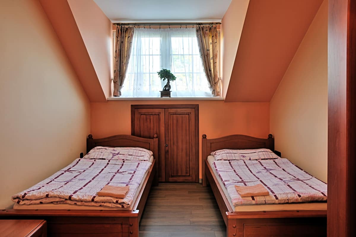 A bedroom with two wooden beds, a window with curtains, and a door.