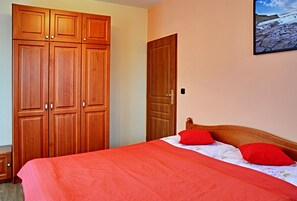 Une chambre à coucher avec un lit, une literie rouge, une armoire en bois et un tableau encadré au mur.