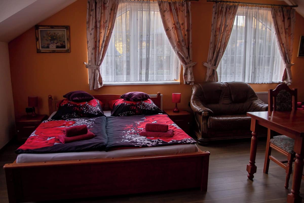 A bedroom with a large bed, two nightstands, a wooden chair, a wooden table, and a window with curtains.