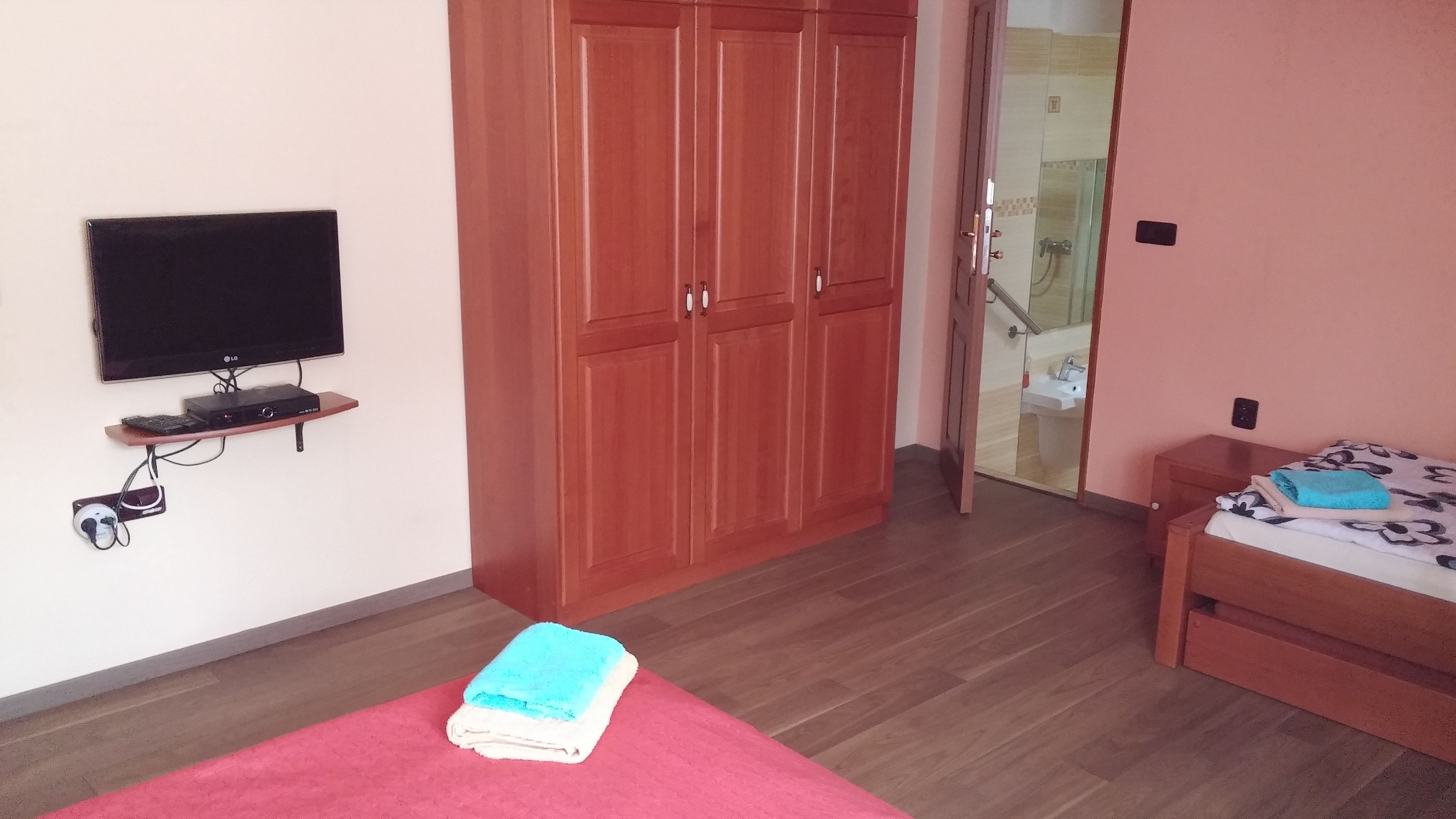 Een slaapkamer met een televisie, een houten garderobe en een bed met een blauwe handdoek.
