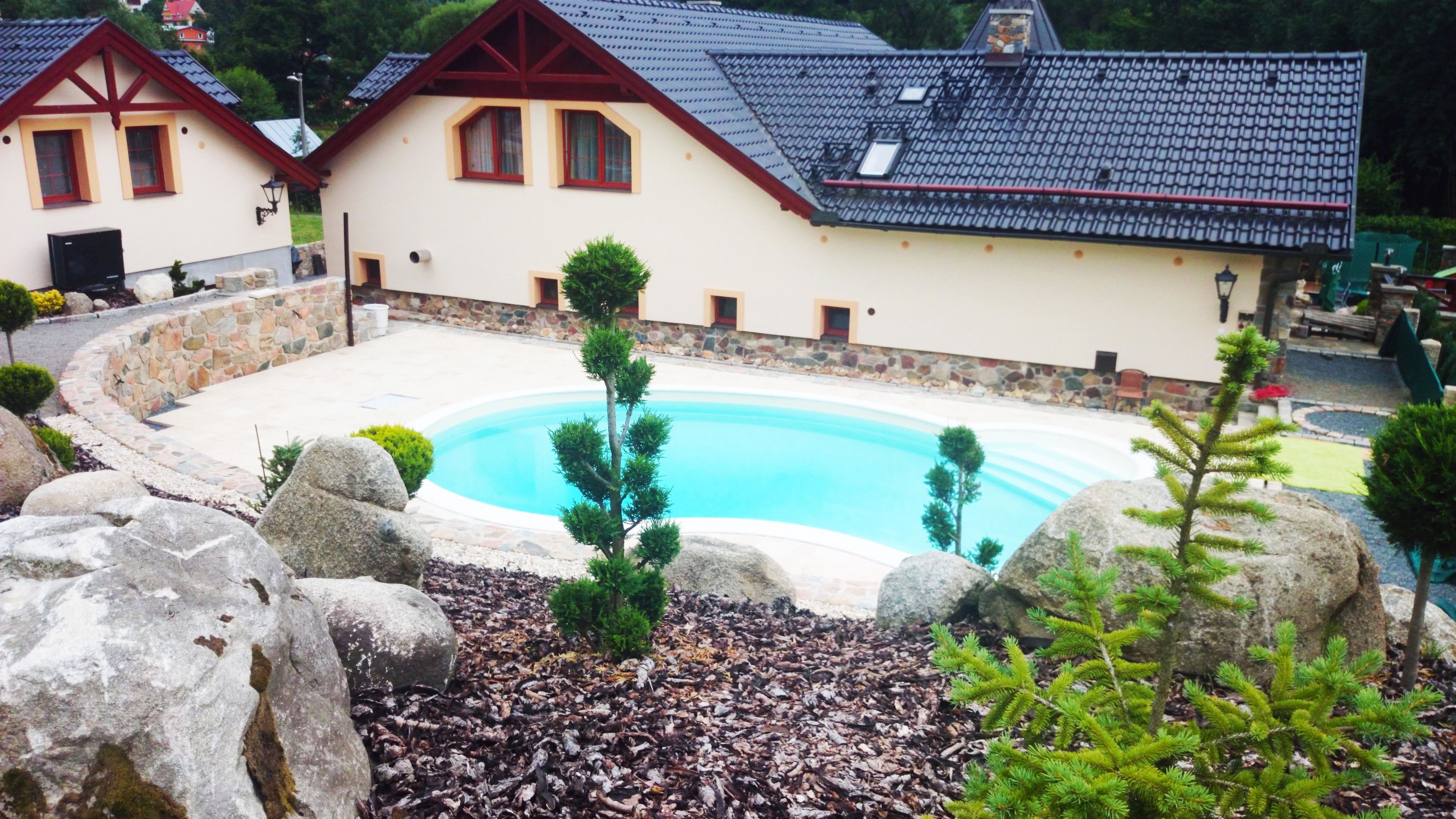 A swimming pool surrounded by rocks and small trees, with a building in the background.