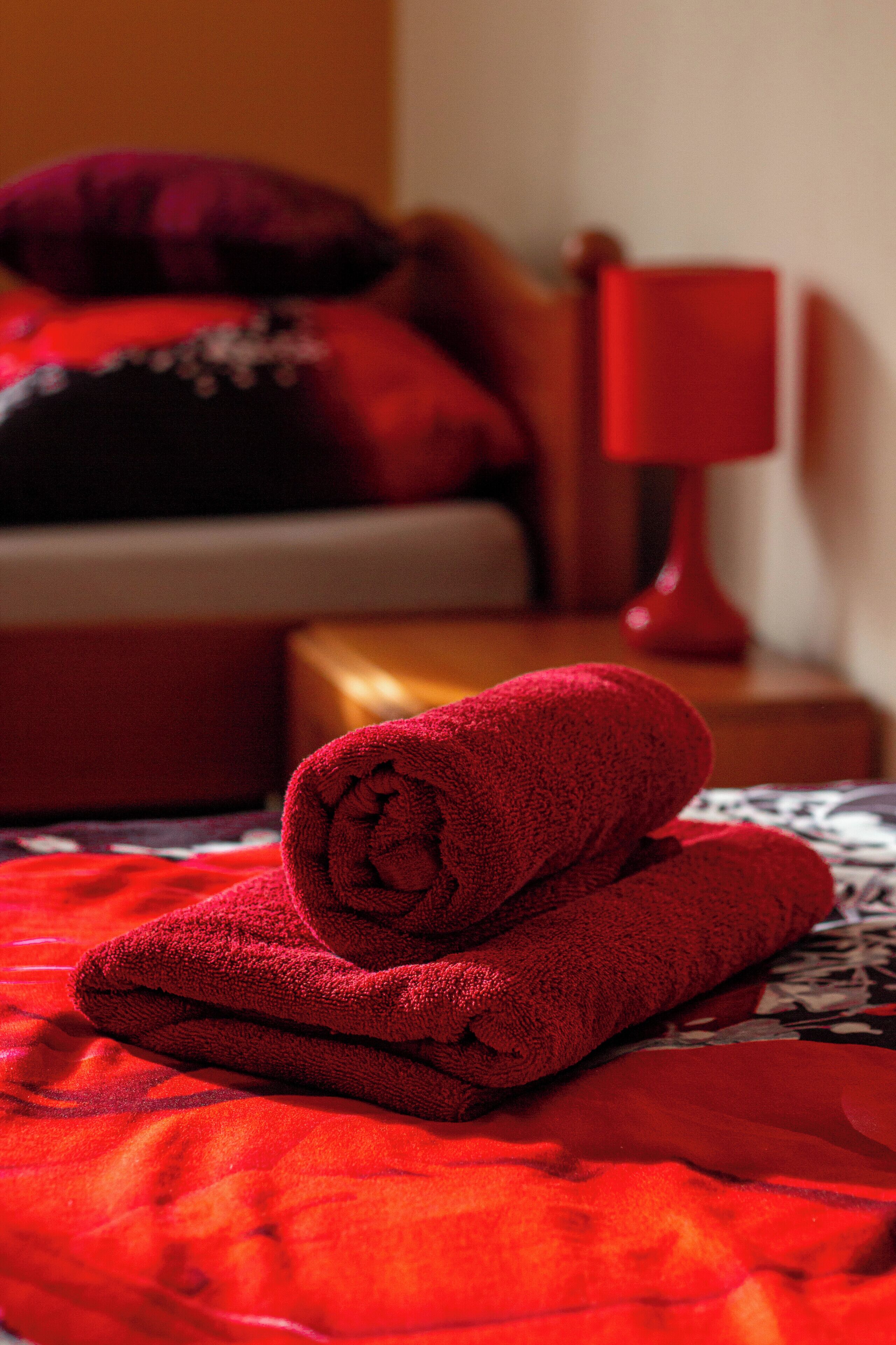 A neatly made bed with a red blanket and pillows, a red bedside lamp, and a wooden nightstand.