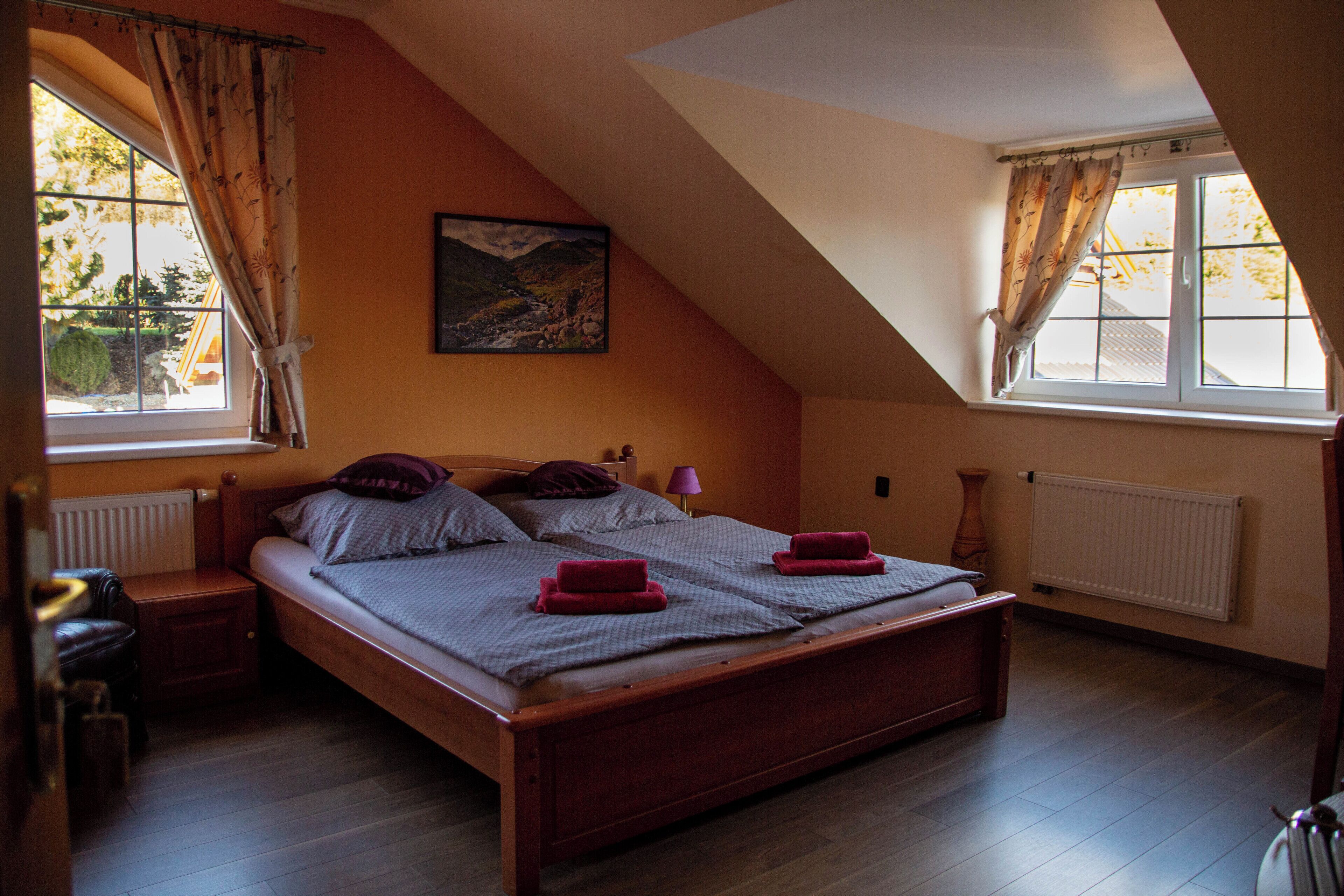 A bedroom with a sloped ceiling, a wooden bed, two nightstands, a lamp, and a painting on the wall.