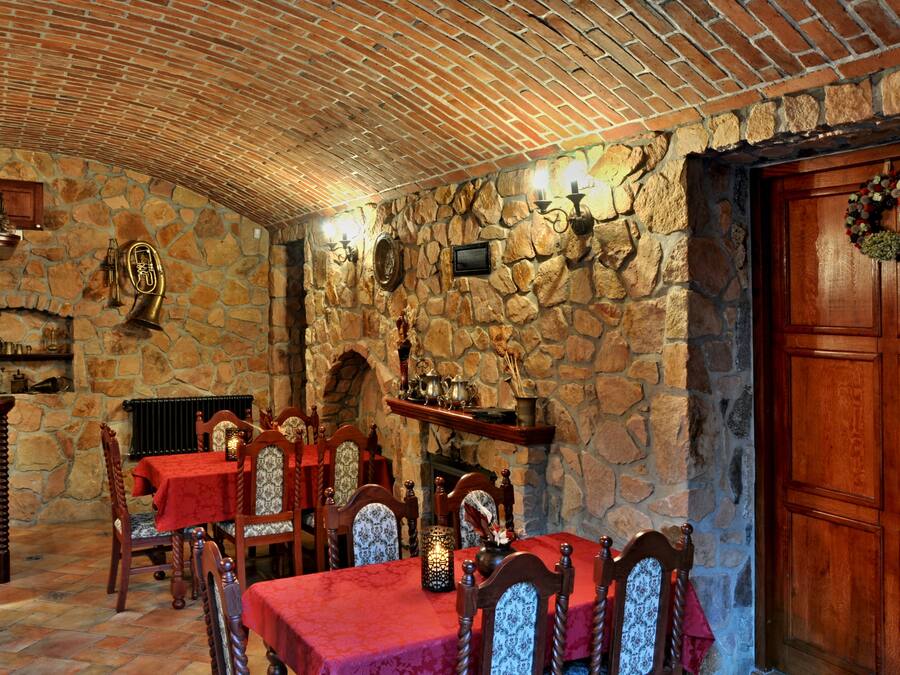 A stone-walled dining area with wooden chairs and tables, a fireplace, and a wooden door with a wreath.
