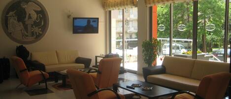 Un vestíbulo de hotel con un sofá, sillas, una mesa de centro, una televisión y un ventanal con vistas a la calle.