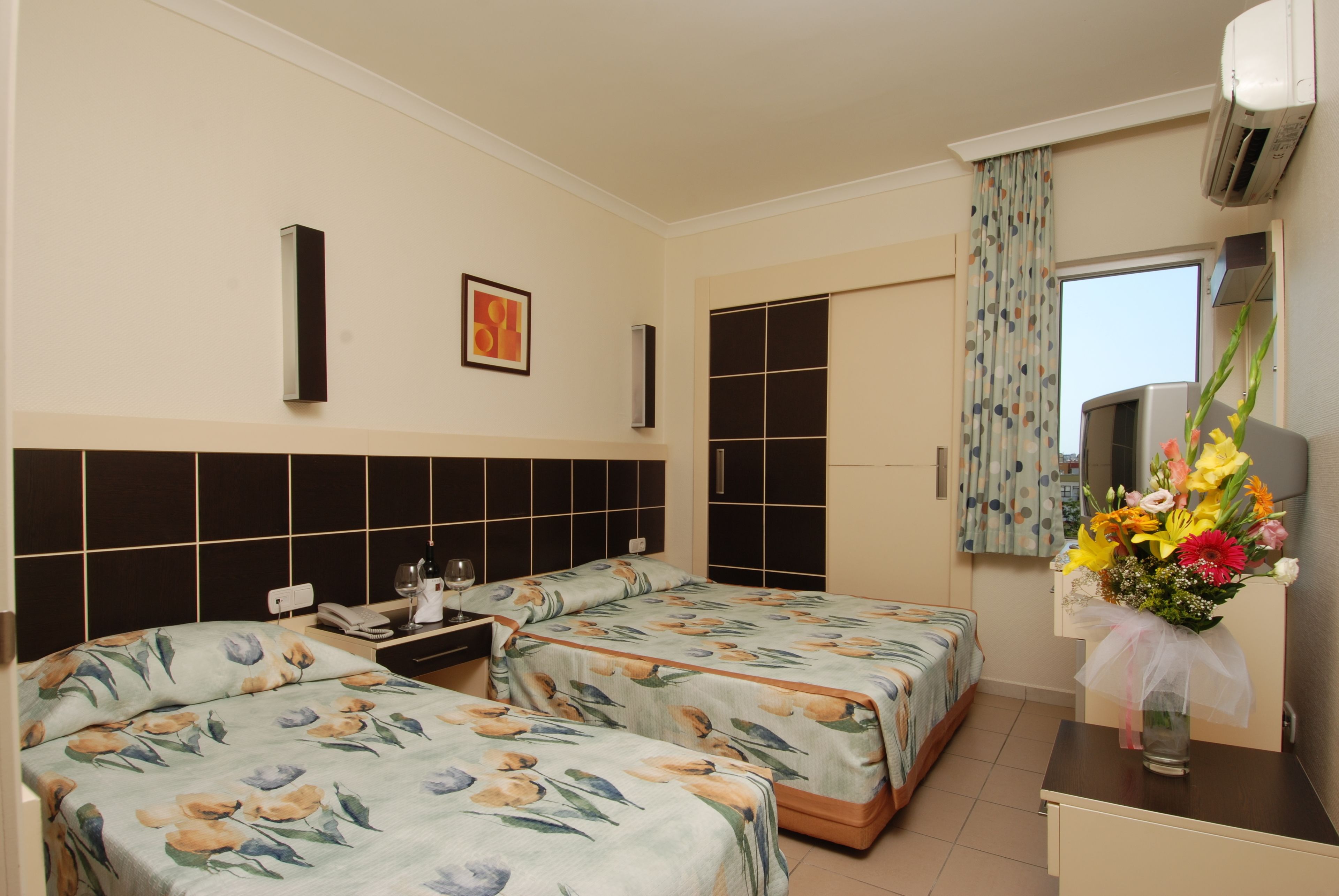 A hotel room with two beds, a desk, a chair, a mirror, and a window with curtains.