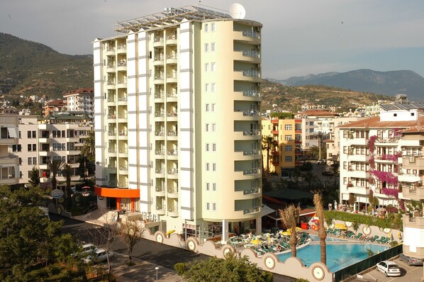 Un hotel a più piani con balconi, una piscina e vista sulla città e sulle montagne circostanti.