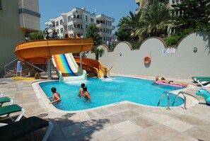A swimming pool with a water slide, lounge chairs, and a lifebuoy on the wall. - Okan Tower Apart Hotel (Alanya)