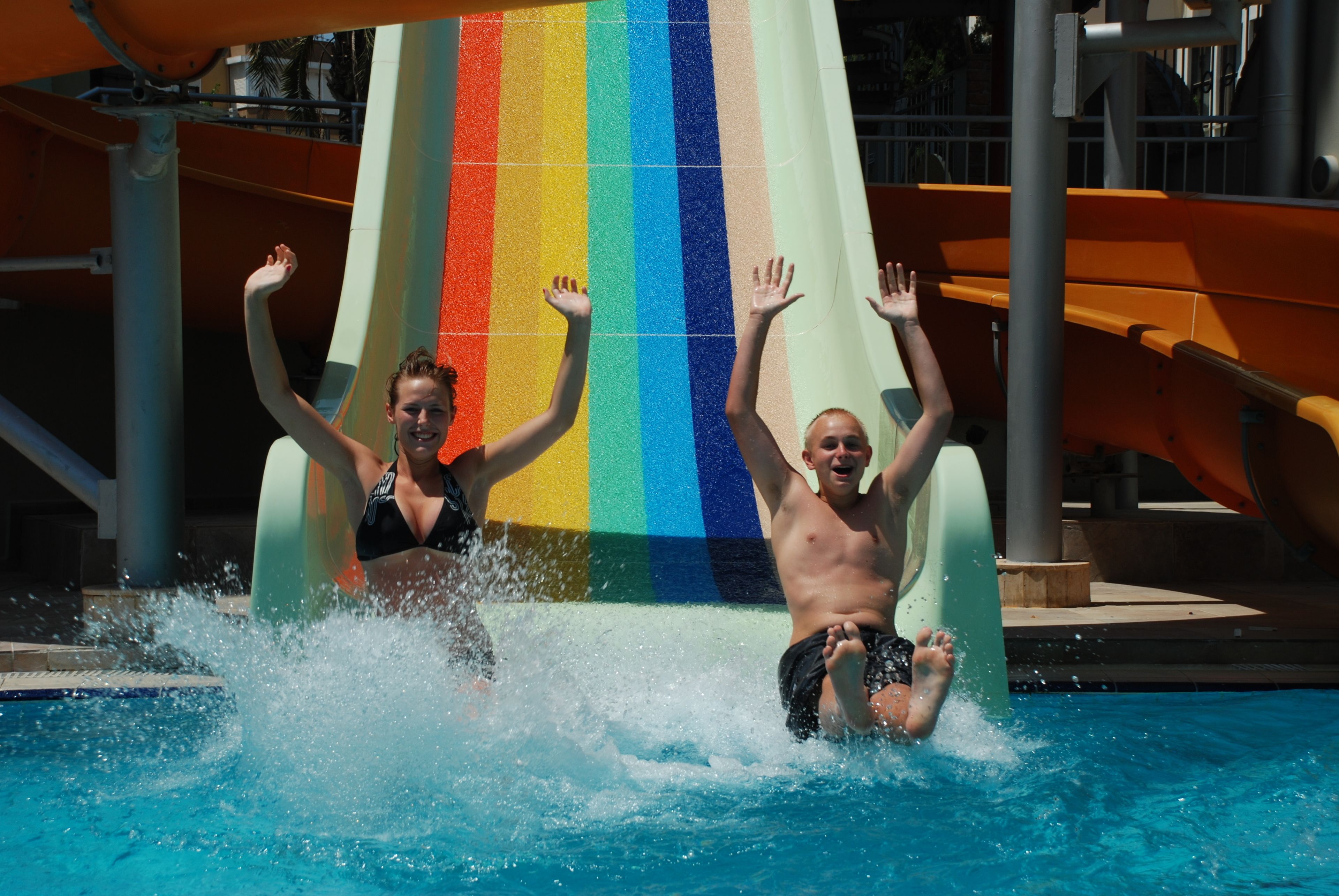 Deux personnes dévalent un toboggan aquatique multicolore et atterrissent dans une piscine.