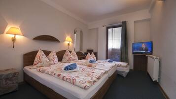 A hotel room with a double bed, two bedside tables, a TV, and a window with curtains.