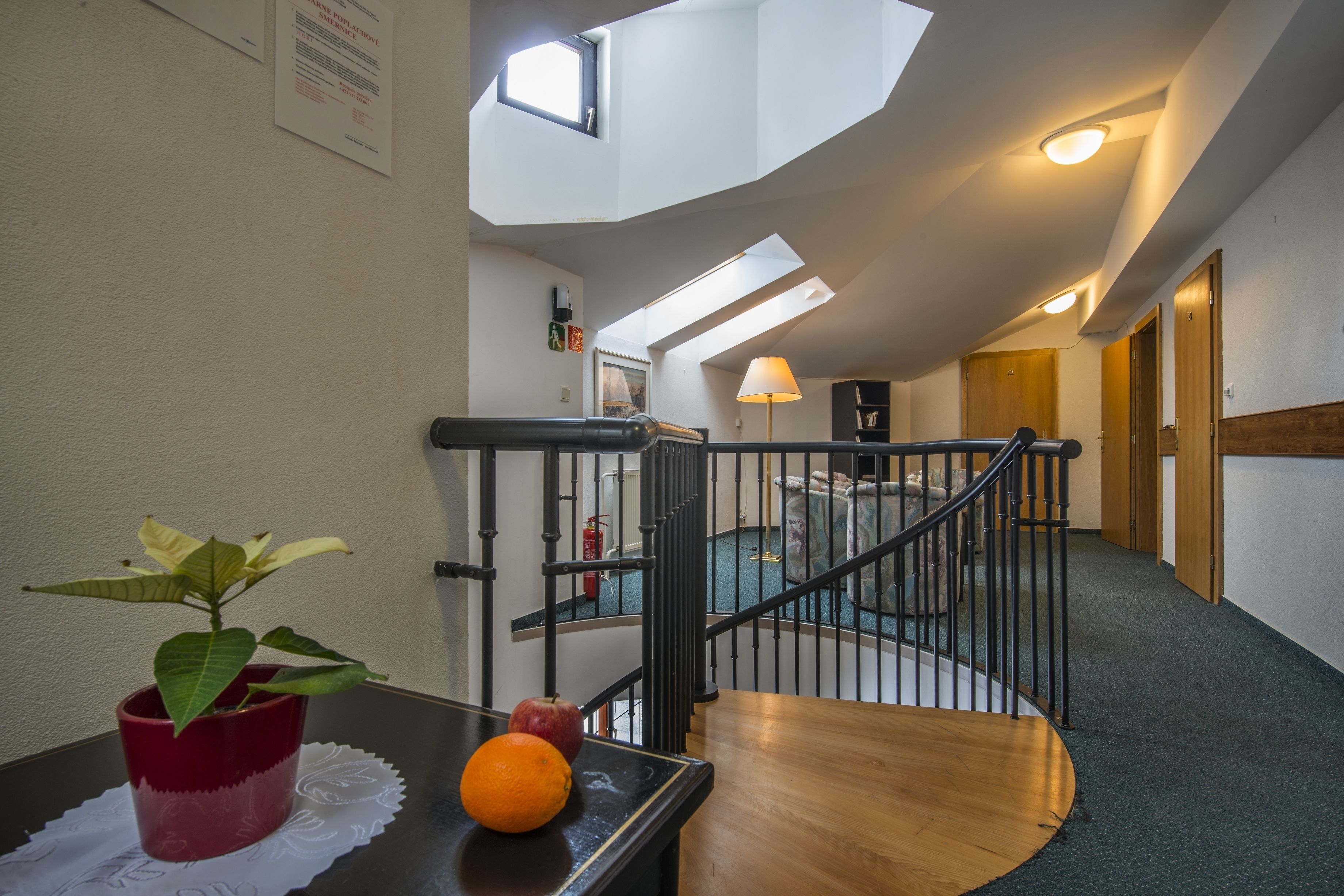 Un escalier avec une rampe en bois et des balustrades en métal noir, menant à une pièce dotée d’une fenêtre et d’une lampe posée sur une table.