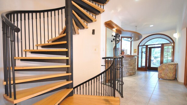 A modern interior with a spiral staircase, stone fireplace, and a view through a glass door. - Penzion Pleso (Štrba)