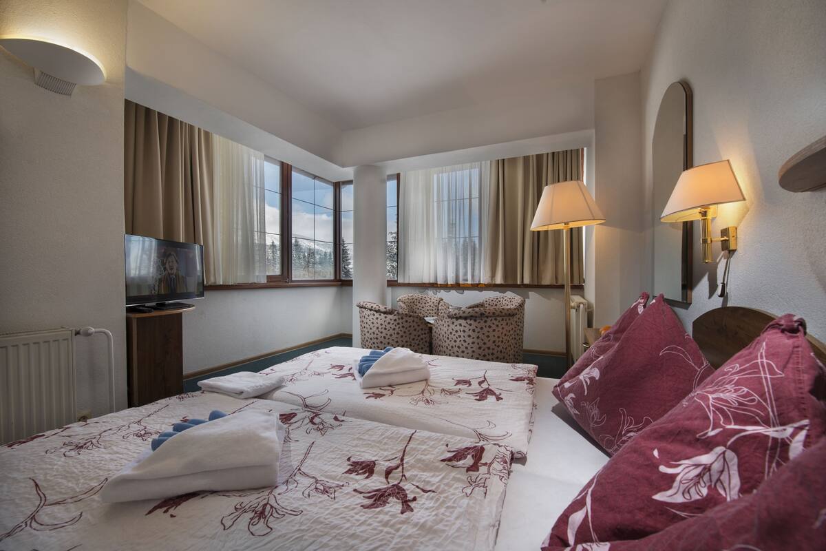 A hotel room with a large bed, two bedside lamps, a TV, and a view of the outdoors.