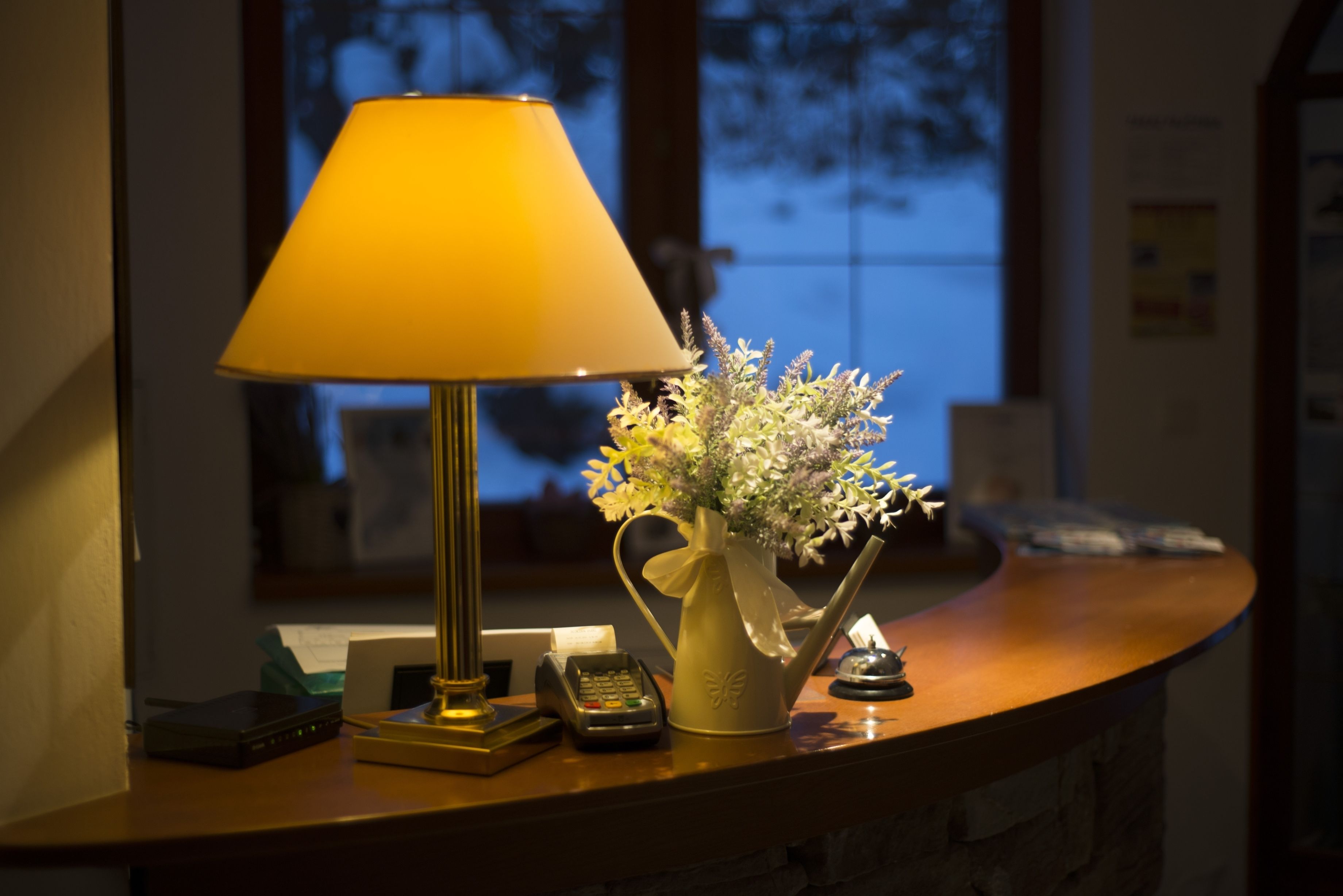 A desk with a lamp, a vase with flowers, a telephone, and a small decorative item.