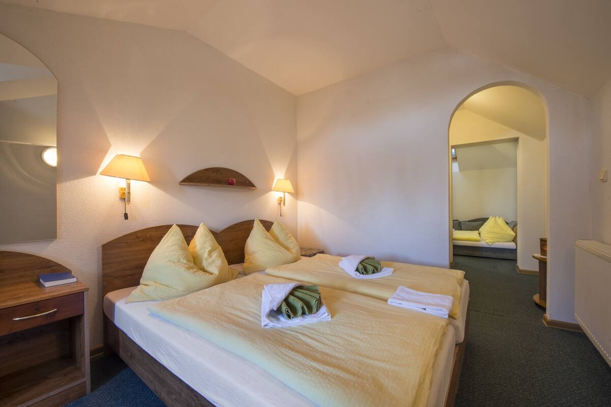 A hotel room with two beds, a wooden headboard, a desk with a book, and two lamps.