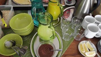 A breakfast table with various food items and drinks, including a green pitcher, a glass of orange juice, and a plate of sliced fruit.