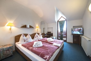 Relax in comfort with a large bed, wall-mounted lamps, and a TV, set against a serene outdoor view.