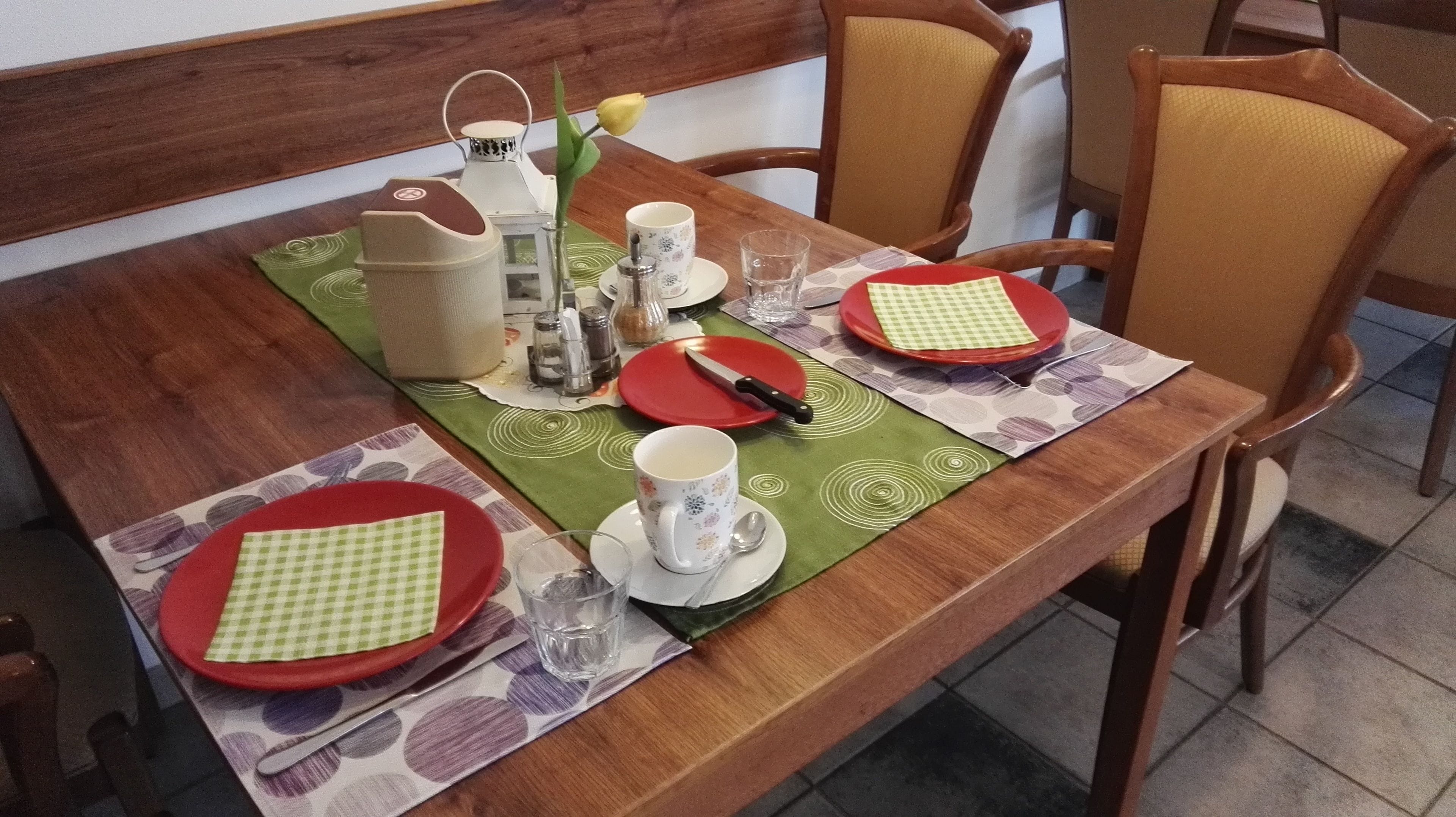 A dining table set with red and green placemats, plates, cups, and cutlery.