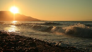 A beach with waves and the sun setting in the background.