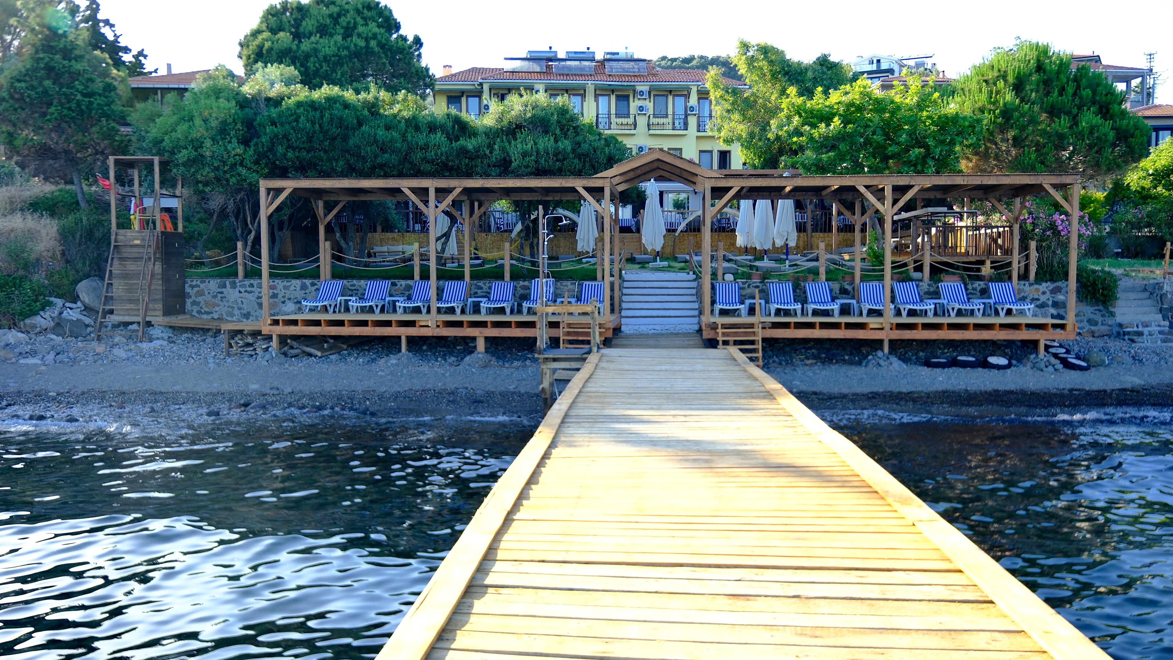 Un muelle de madera que conduce a un área de descanso frente a la playa, con sillas a rayas azules y blancas.