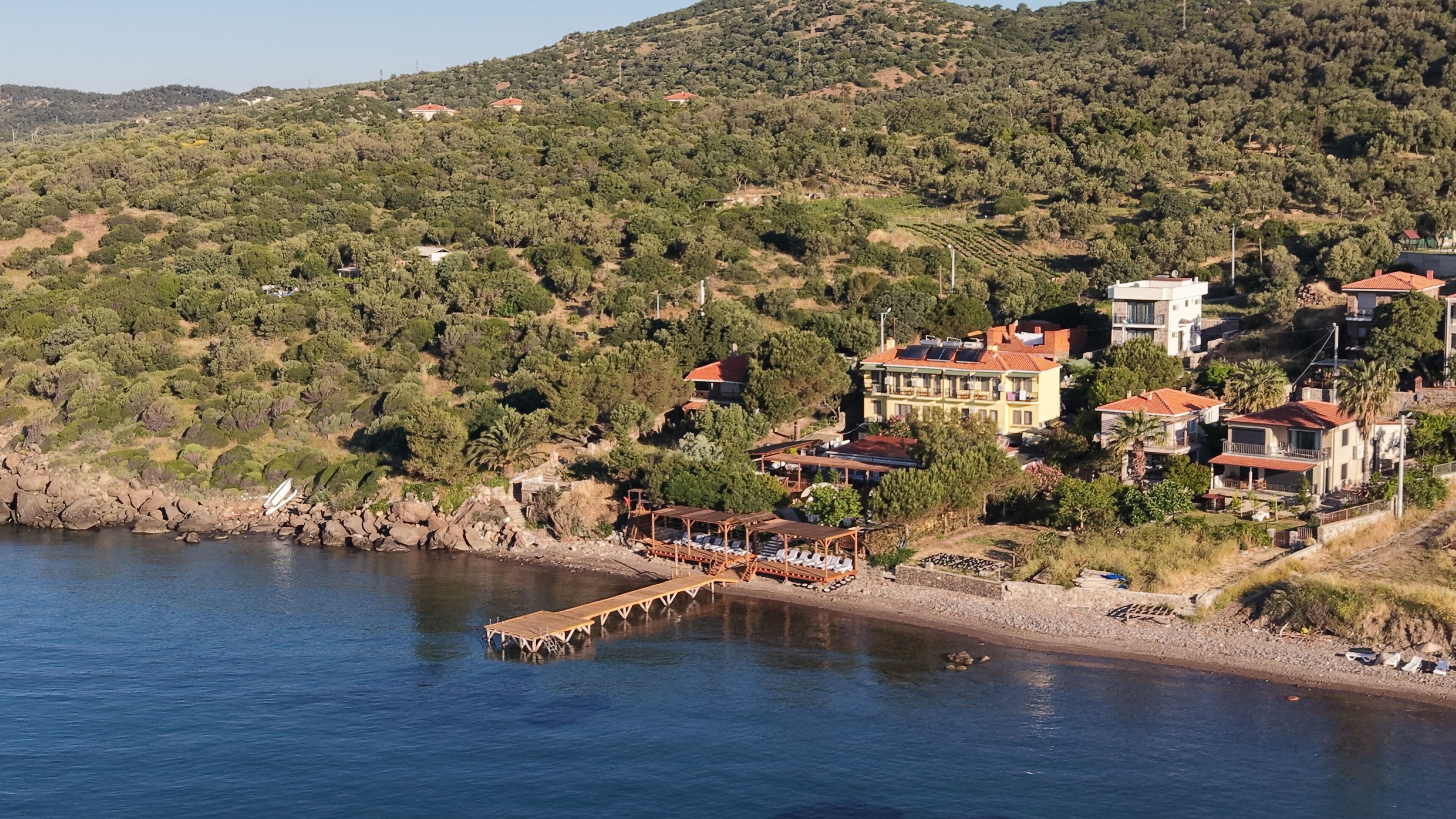 A coastal property with a wooden pier, hillside houses, and a view of the sea.
