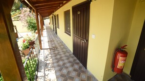 A covered corridor with a tiled floor, wooden ceiling, and a fire extinguisher mounted on the wall.