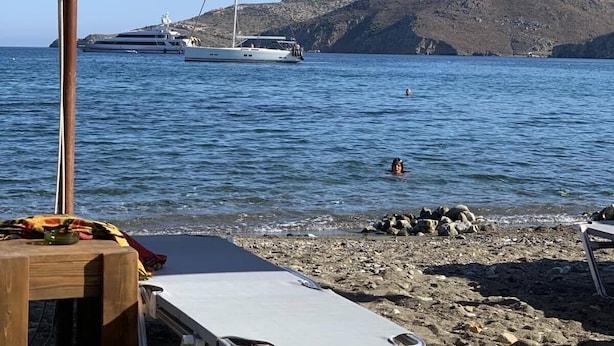 A beach with umbrellas, a rocky shoreline, and a sailboat in the background. - Gerani Studios (Astypalaia)