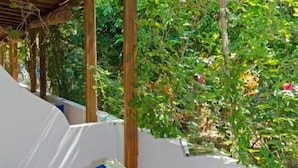 A covered outdoor seating area with a table set for breakfast, surrounded by lush greenery. - Gerani Studios (Astypalaia)