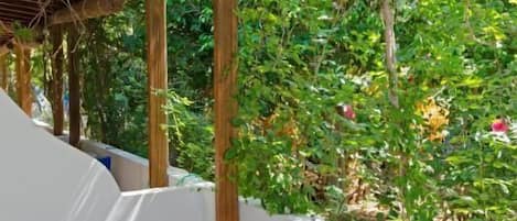 A covered outdoor seating area with a table set for breakfast, surrounded by lush greenery.