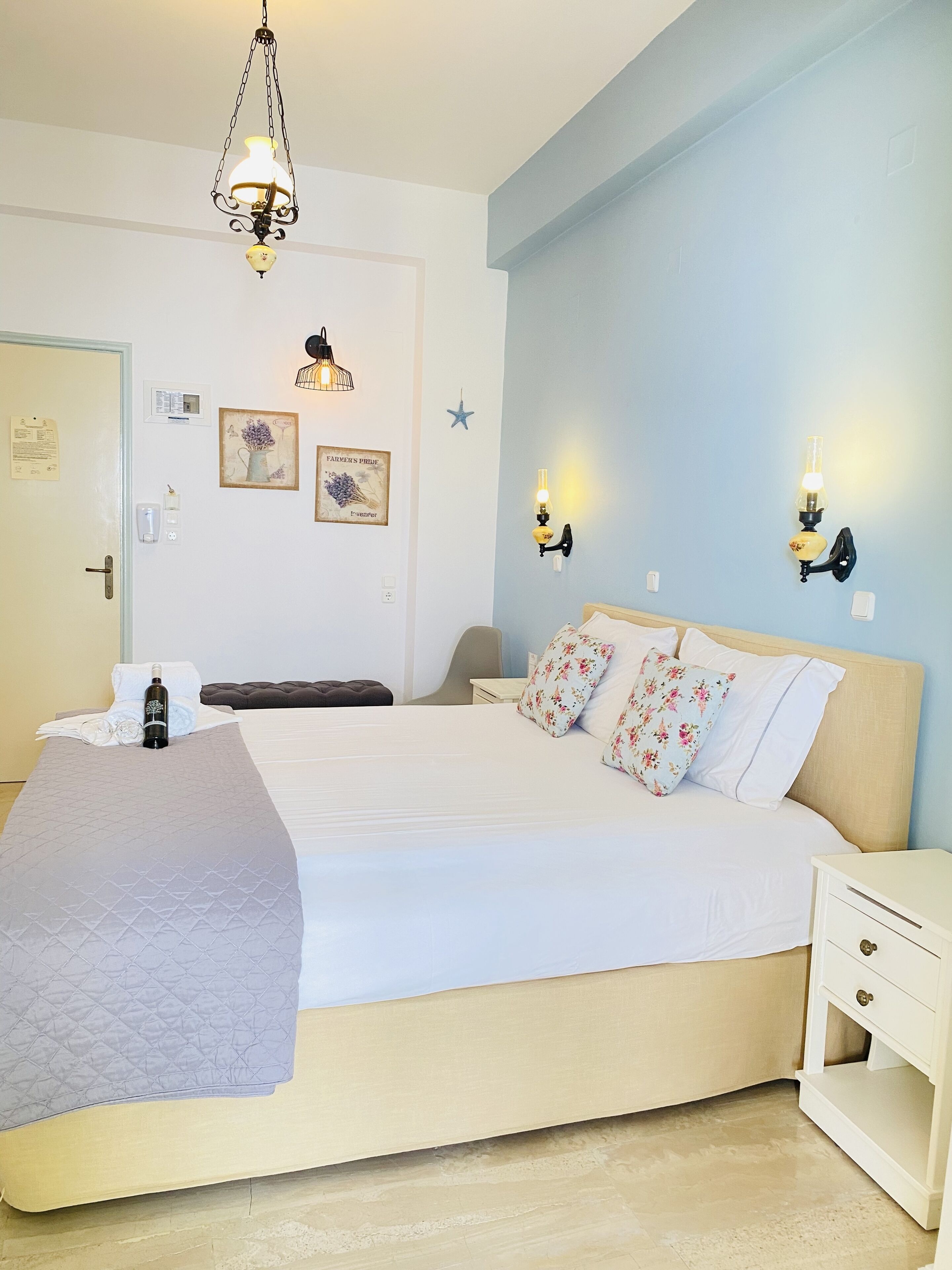 A bedroom with a bed, bedside tables, a hanging light fixture, wall-mounted lights, and a door with a notice.