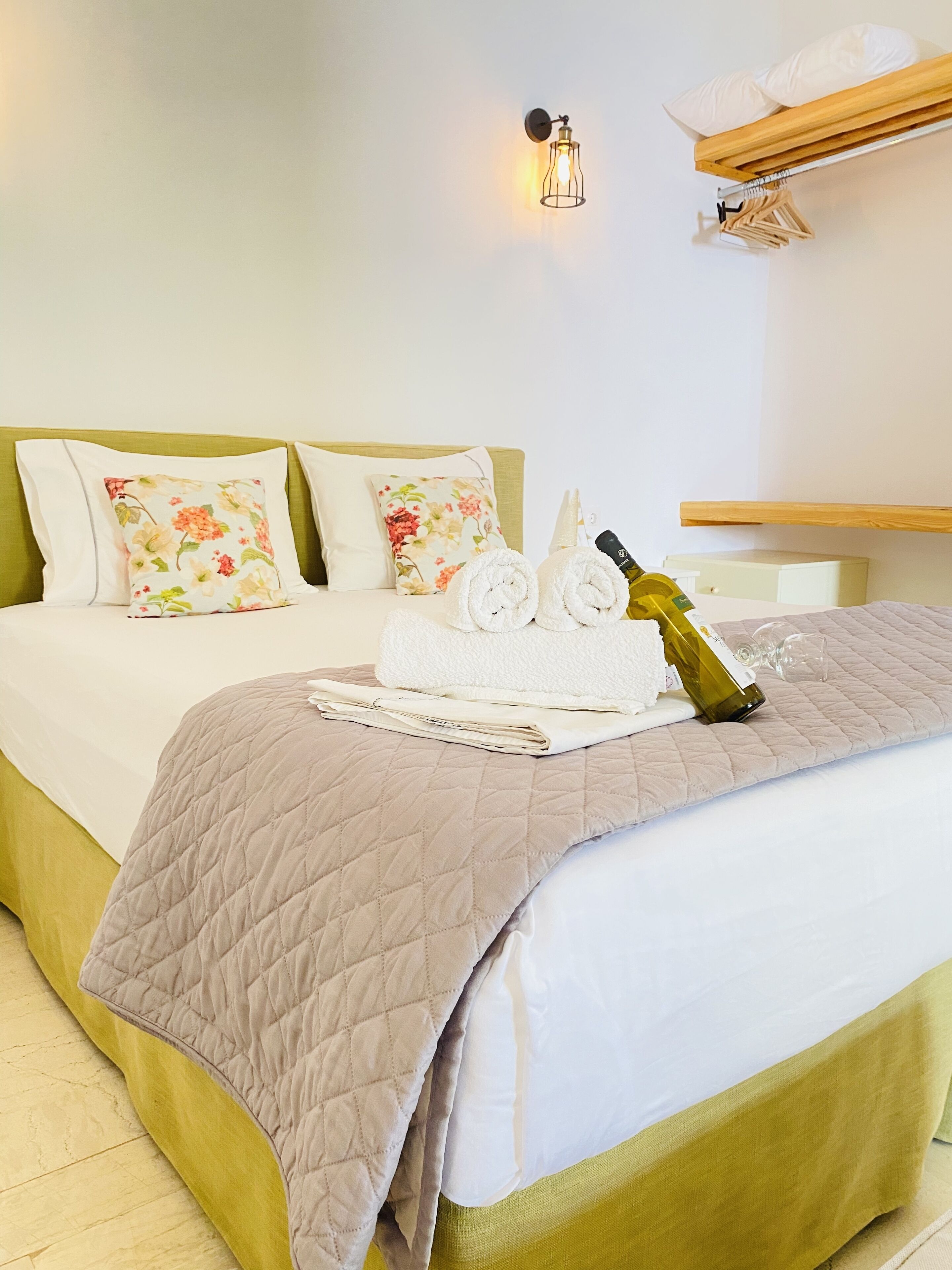 Una cama bien hecha con una cubierta acolchada, dos toallas enrolladas, una botella de vino y una almohada estampada.