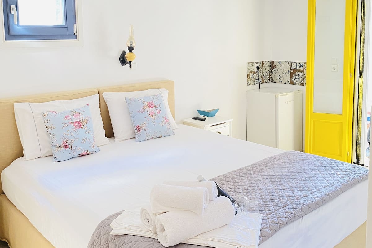 A neatly made bed with floral pillows, a quilted blanket, and rolled towels.