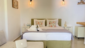 A bedroom with a bed, a bedside table, a lamp, a laptop, and a small table with a bottle and glasses. - Gerani Studios (Astypalaia)