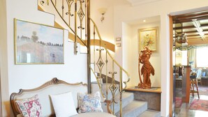 A staircase with ornate metal railings, a cushioned bench with patterned cushions, and a statue on the landing. - Hotel Karin (Tirolo)