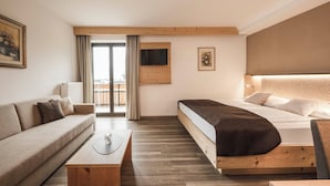 A modern hotel room with a wooden bed, a sofa, a coffee table, and a TV on the wall. - Hotel Karin (Tirolo)