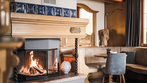 A modern living room with a fireplace, a wooden mantel, and a seating area with a sofa and a chair. - Hotel Karin (Tirolo)