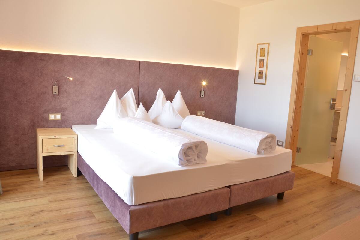A modern hotel room with a large bed, a bedside table, and a wooden headboard.