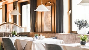 A restaurant with wooden ceiling beams, white tablecloths, and grey upholstered chairs. - Hotel Karin (Tirolo)