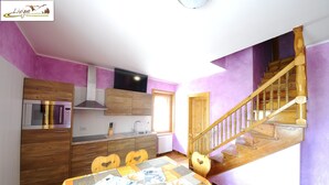 A kitchen with wooden cabinets, a microwave, and a sink. There is a dining table with chairs and a staircase with wooden steps. - Residence Casa Longa (Livigno)