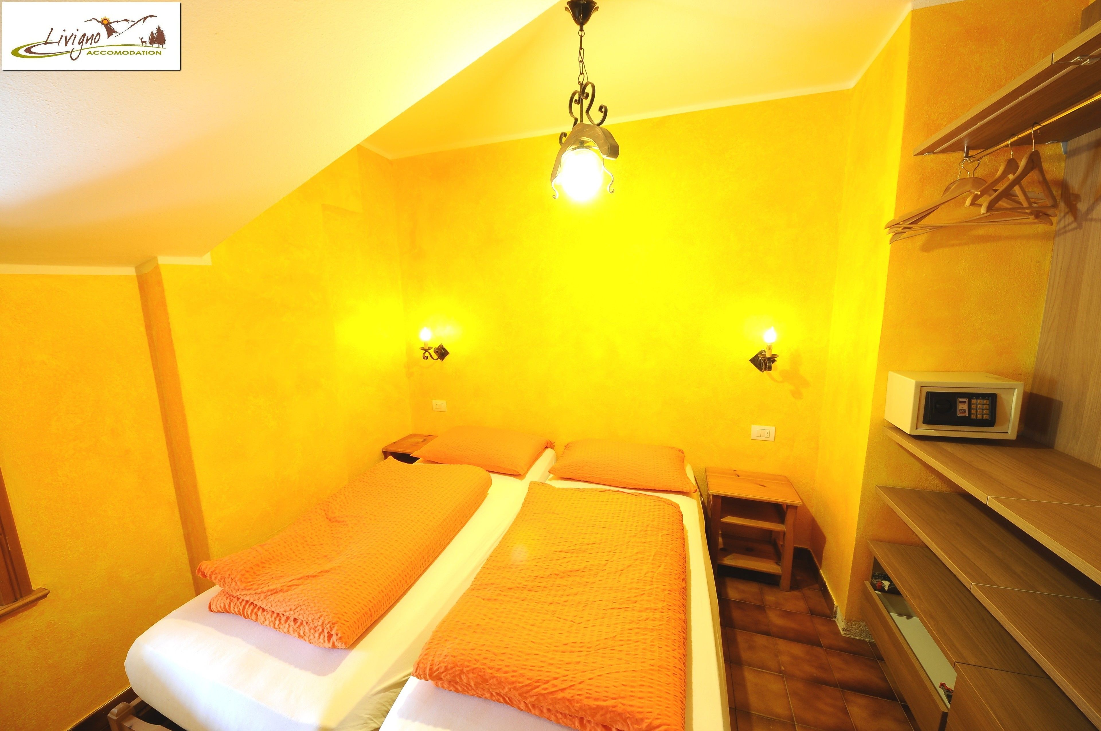 A room with two beds, a wooden bench, a microwave, and a hanging clothes rack.