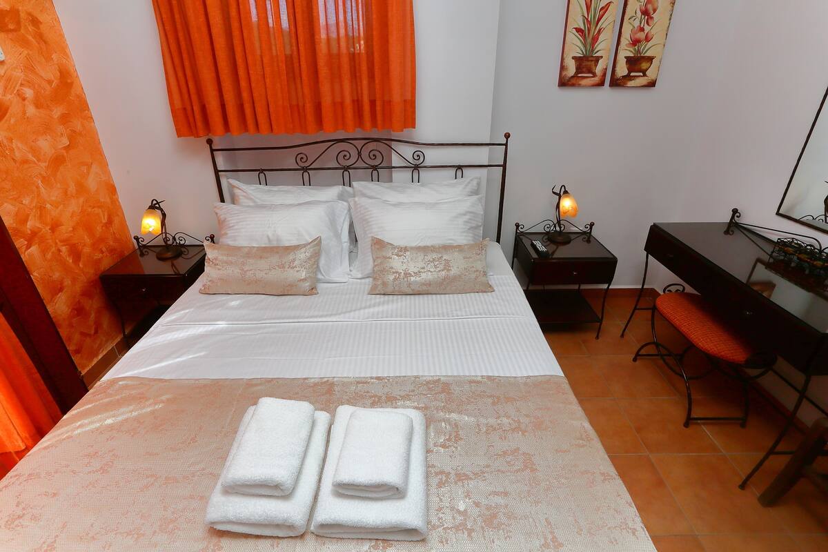 A neatly made bed with white linens and two pillows, a desk with a chair, and two bedside tables with lamps.