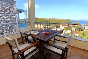 Une table en bois avec des chaises, un livre, un verre et un fruit, le tout sur un balcon donnant sur un paysage magnifique.