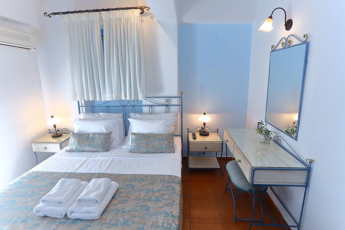 A bedroom with a bed, bedside tables, a desk, a chair, a mirror, and a window with curtains.