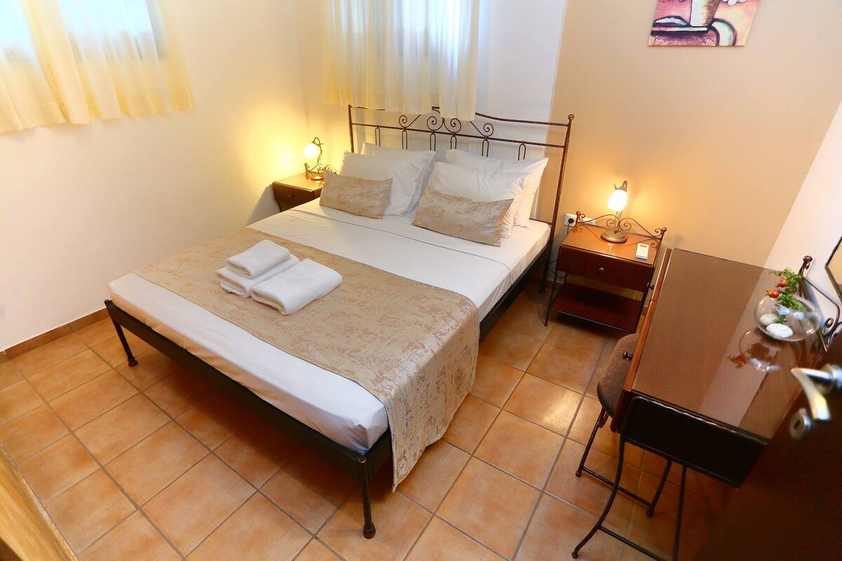 A neatly made bed with a white and beige bedspread, two bedside lamps, and a small table with a lamp beside the bed.