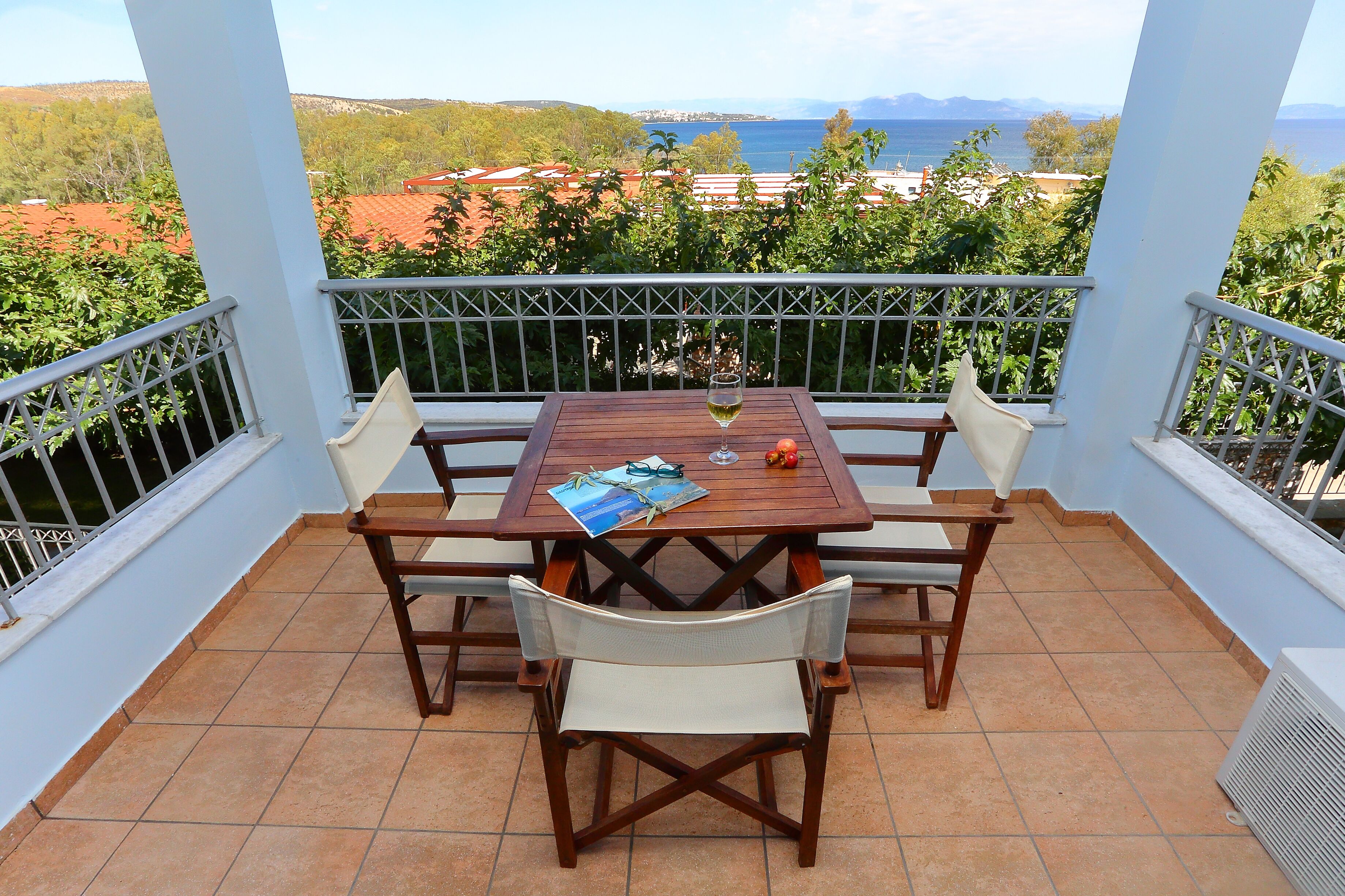 A balcony with a wooden table and chairs, a glass of wine, and a magazine.