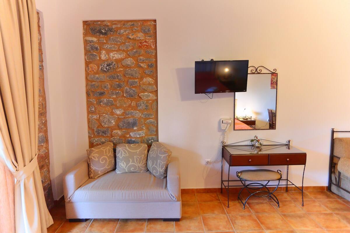 A room with a sofa, a stone wall, a TV, a desk, and a mirror.