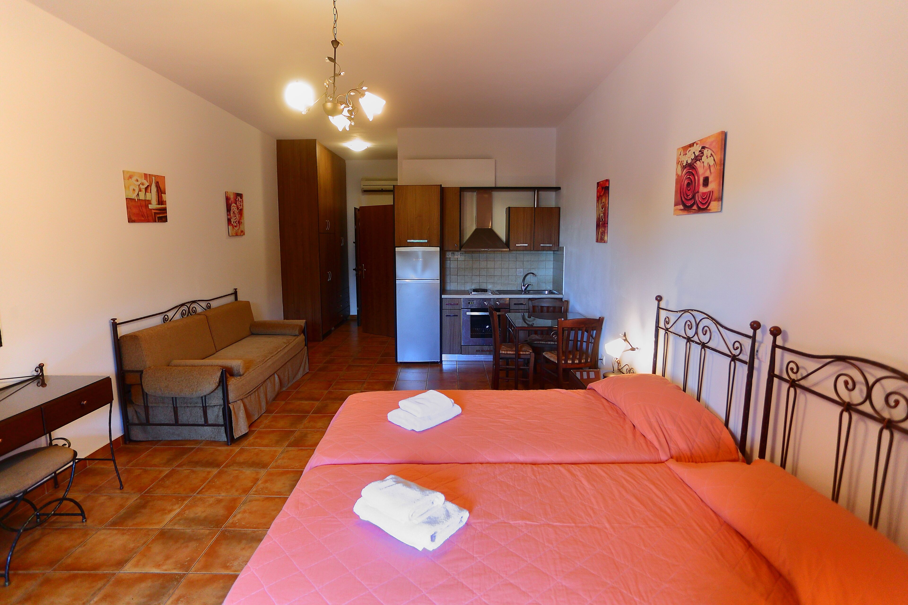 A compact room with a bed, a sofa, a desk, and a kitchenette.