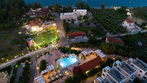 An aerial view of a coastal resort with a swimming pool, outdoor seating, and a colorful play area. - Vathi Hotel (East Mani)