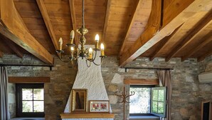 A rustic room with a stone fireplace, wooden beams, a blue armchair, and a chandelier. - Bahab Guest House (Soke)